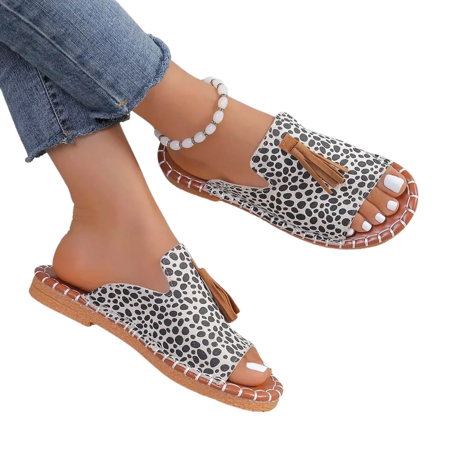 Chinelo slide feminino sendo usado por uma pessoa. O calçado possui uma tira larga com detalhe de borla e uma sola com costura contrastante.