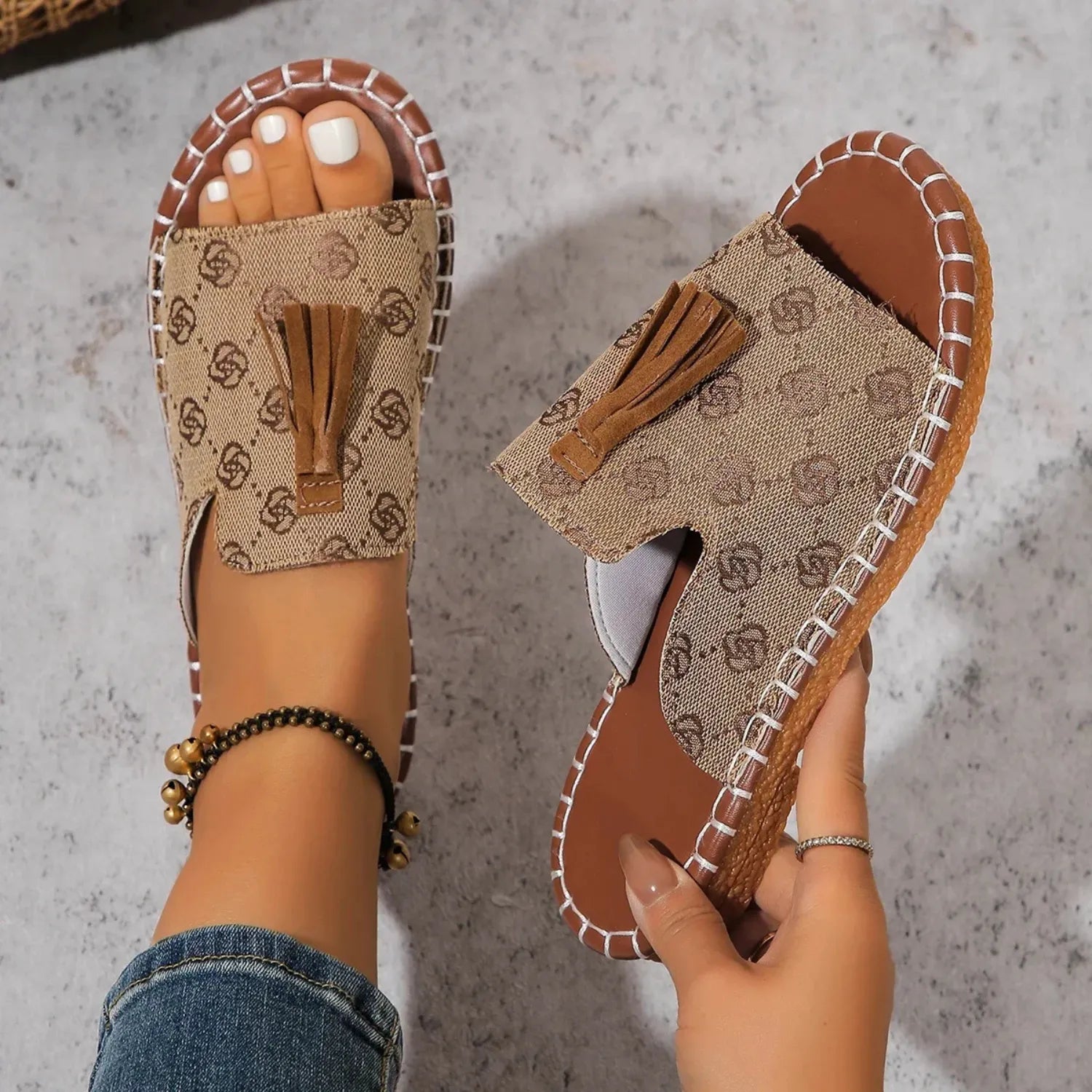 Chinelo slide feminino na cor marrom. O calçado possui uma tira larga com detalhe de borla e uma sola com costura contrastante, ideal para estilo e conforto.