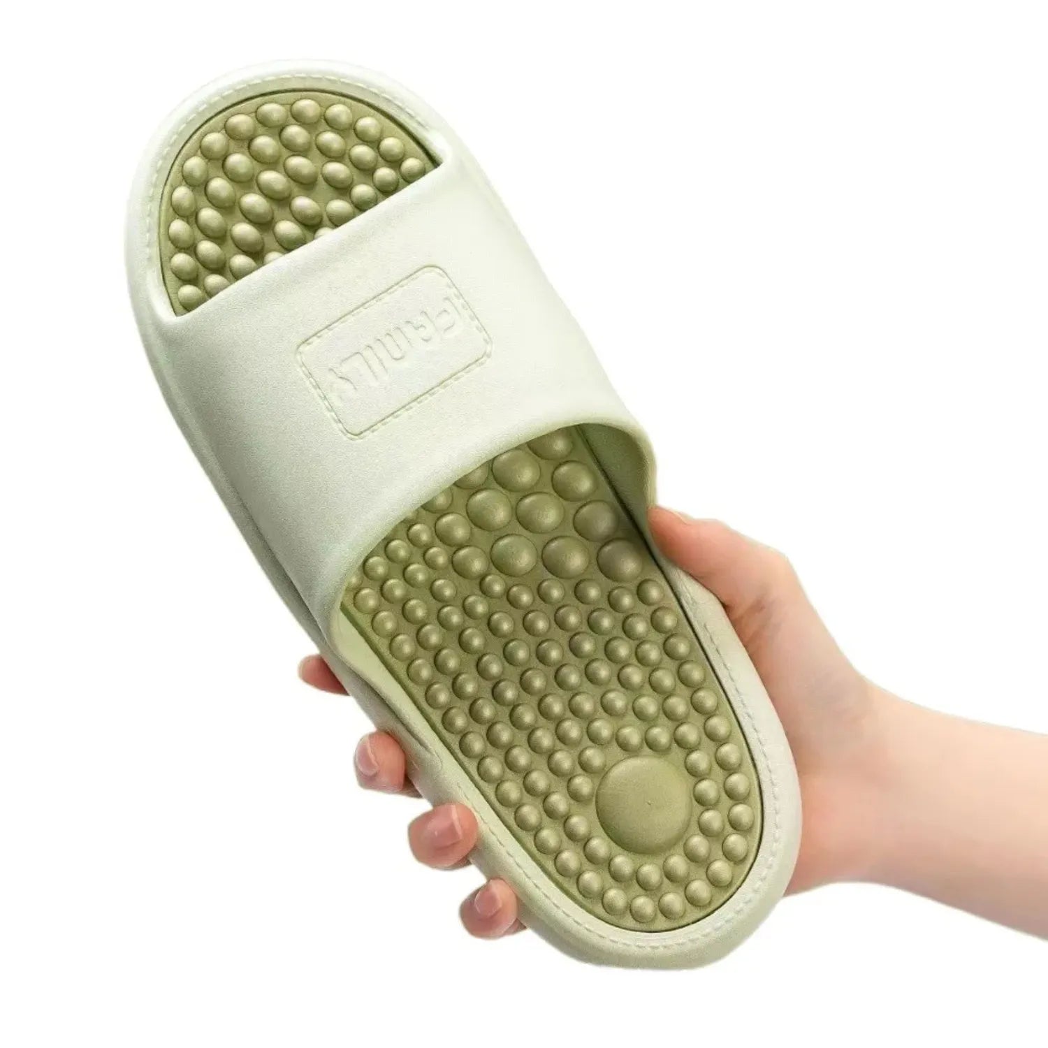 Uma mão segura um chinelo de massagem. O calçado tem uma sola com pontos de massagem elevados e um design antiderrapante para conforto e terapia nos pés.