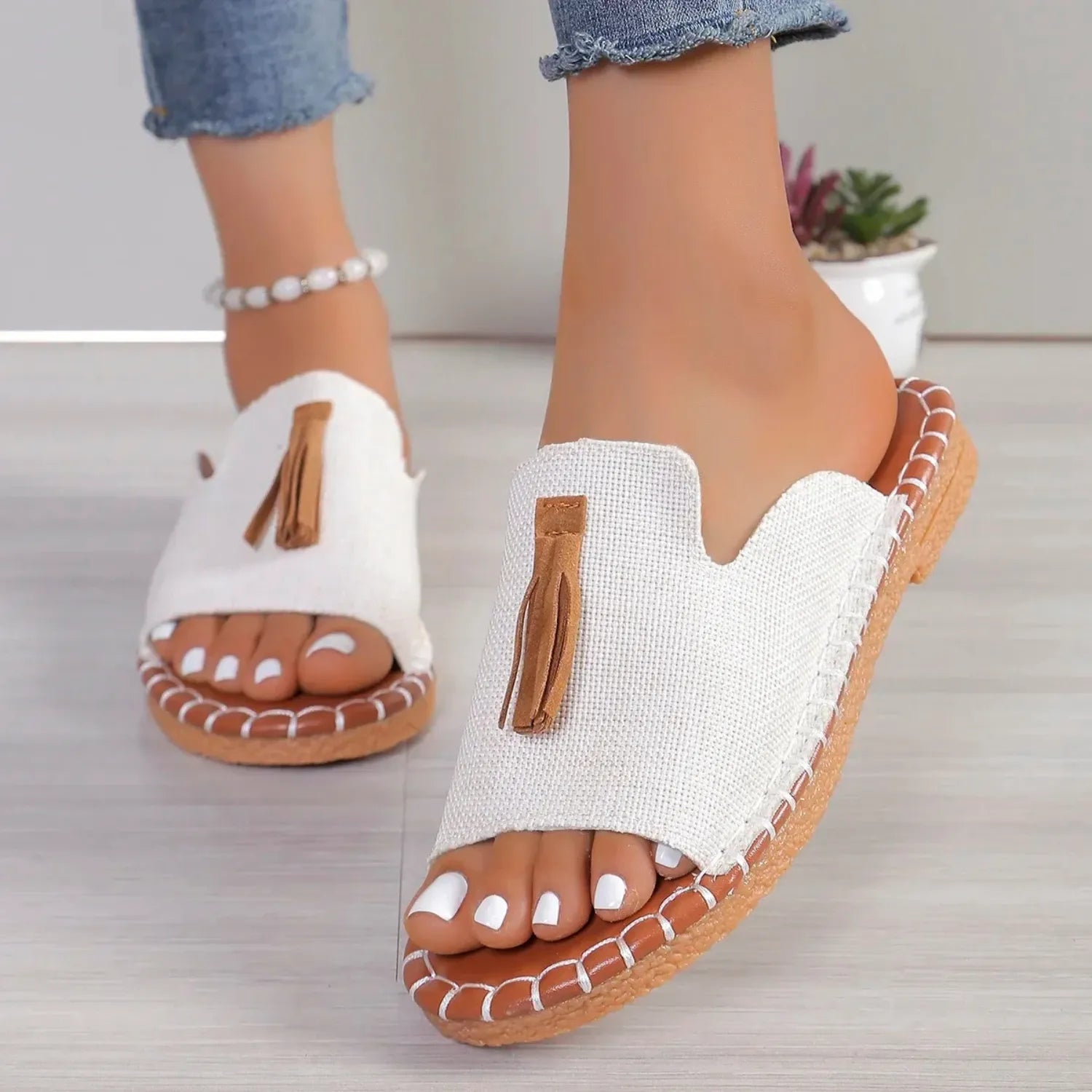 Chinelo slide feminino sendo usado por uma pessoa. O calçado possui uma tira larga com detalhe de borla e uma sola com costura contrastante, com estilo e conforto.