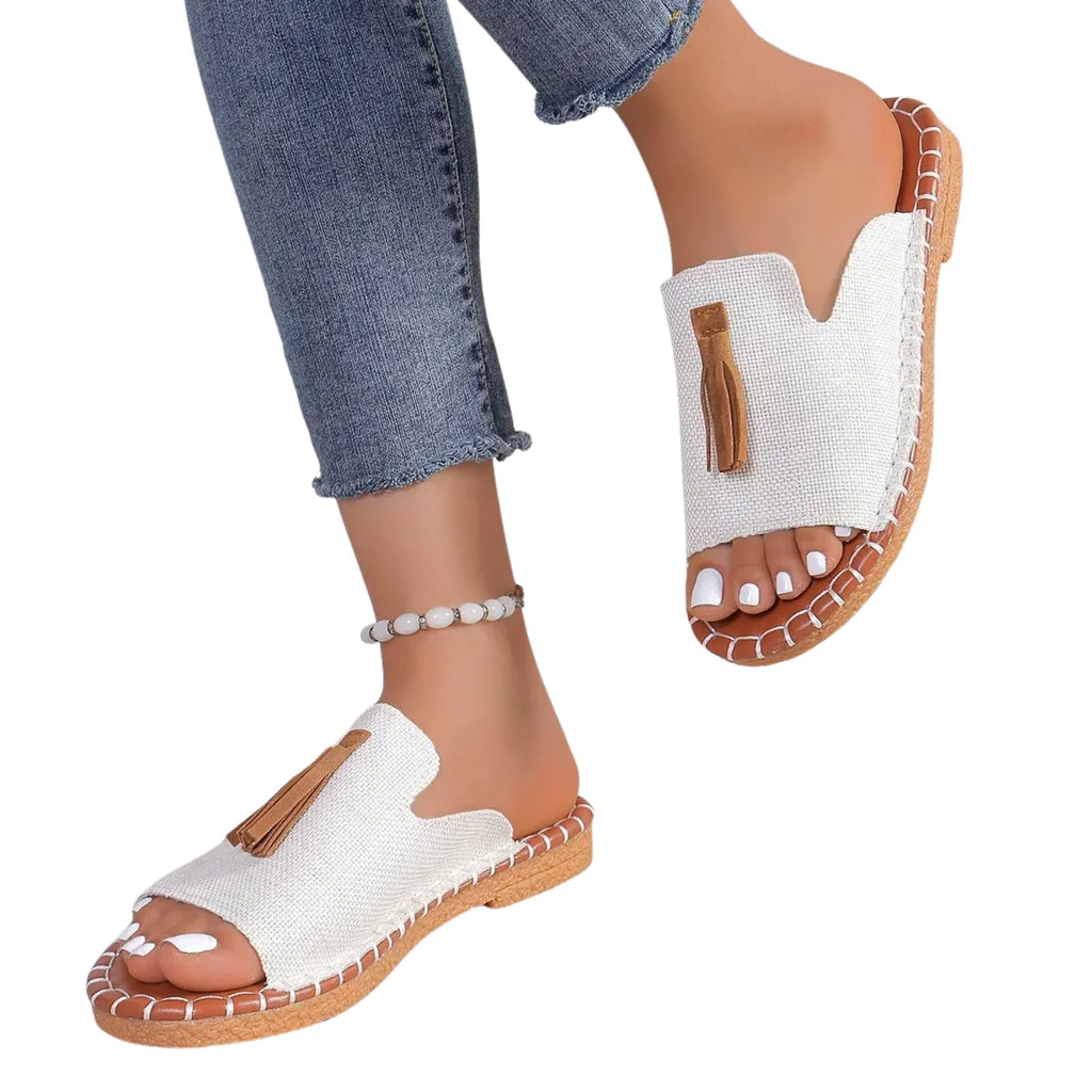 Chinelo slide feminino branco, sendo usado por uma pessoa. O calçado possui uma tira larga com detalhe de borla e uma sola com costura contrastante, ideal para estilo e conforto.