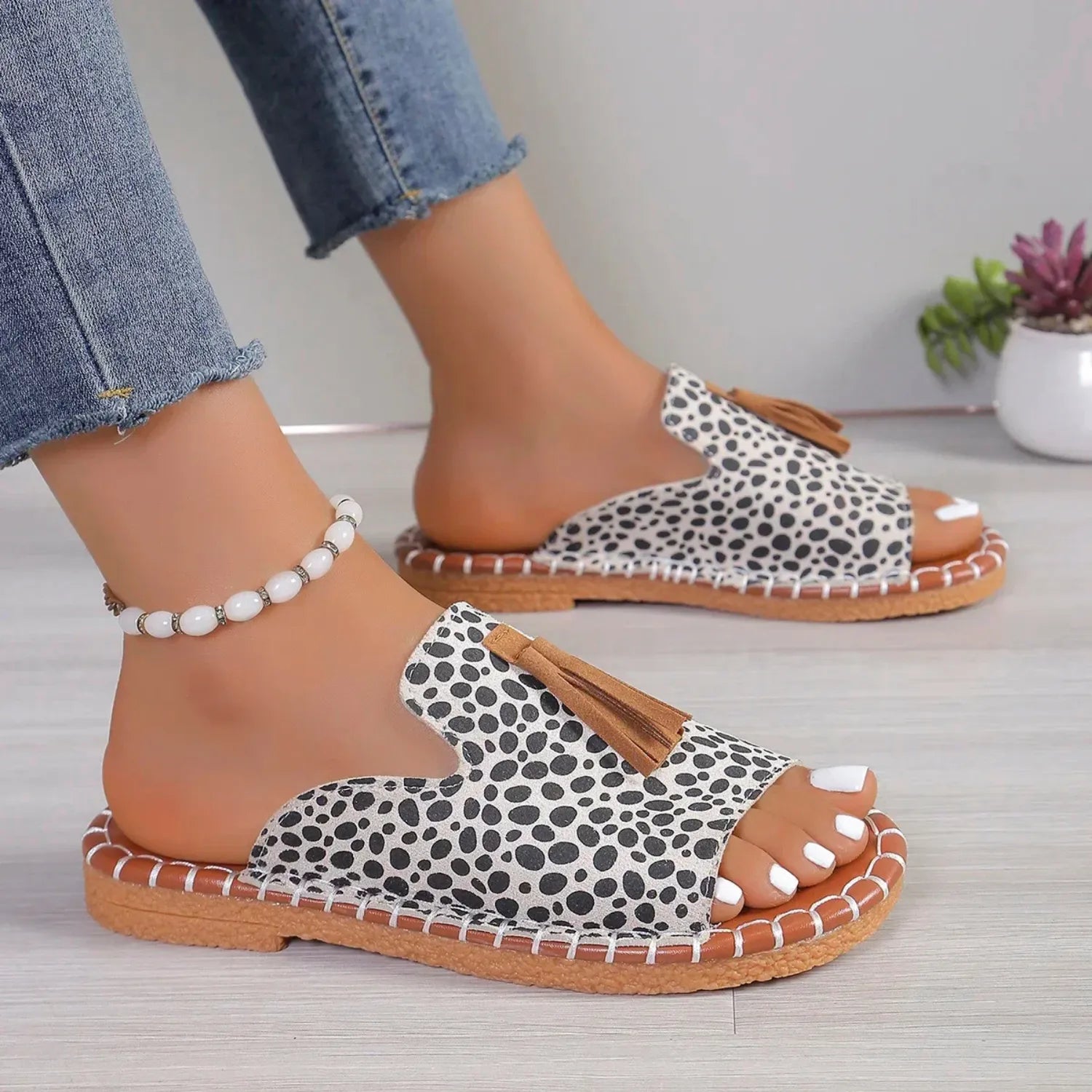 Chinelo slide feminino sendo usado por uma pessoa. Possui uma tira larga com detalhe de borla e uma sola com costura contrastante, ideal para estilo e conforto.