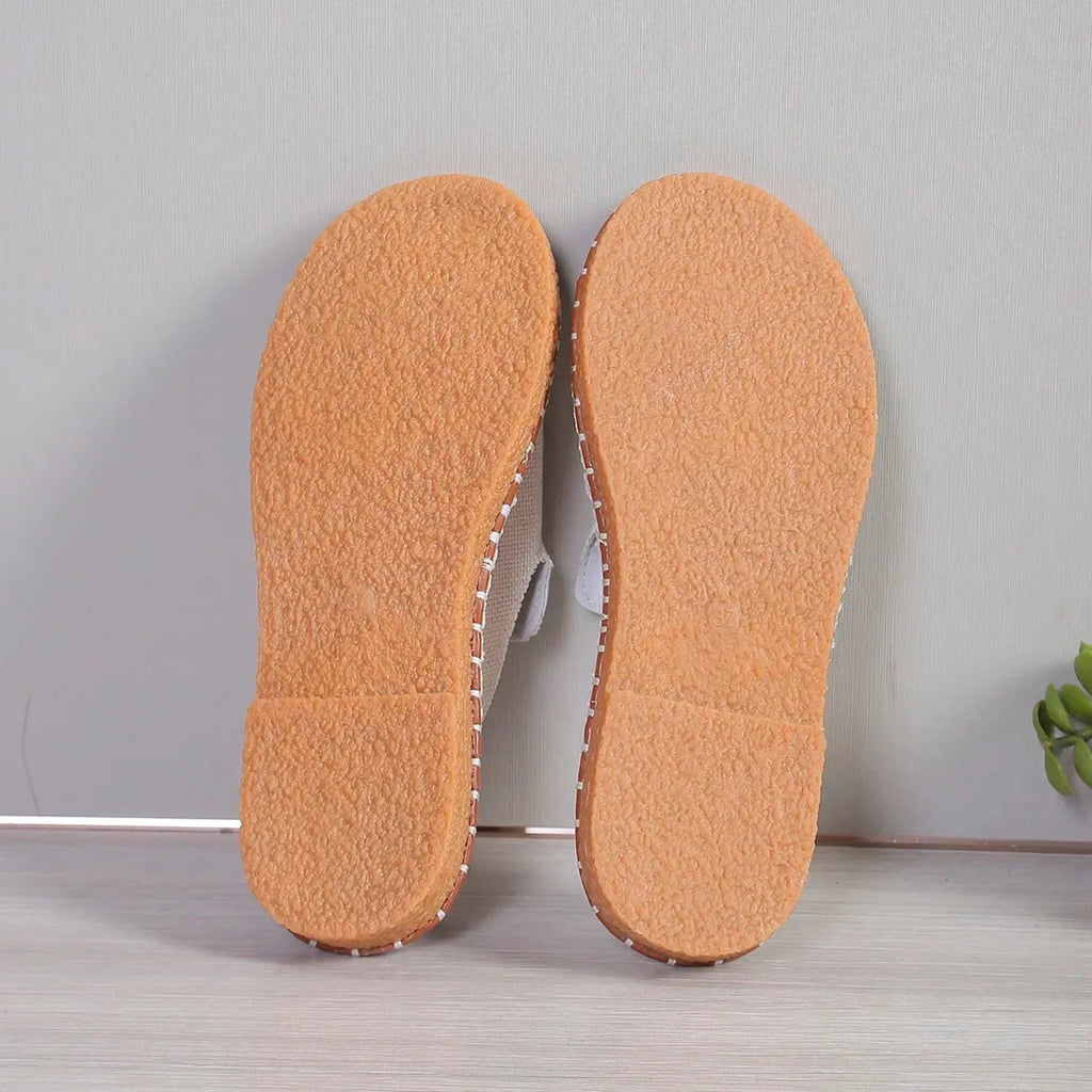 Chinelo slide feminino. O calçado possui uma tira larga com detalhe de borla e uma sola com costura contrastante, ideal para estilo e conforto.