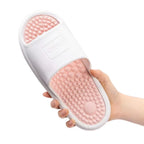 Uma mão segura um chinelo de massagem na cor rosa. O calçado tem uma sola com pontos de massagem elevados e um design antiderrapante para conforto e terapia nos pés.