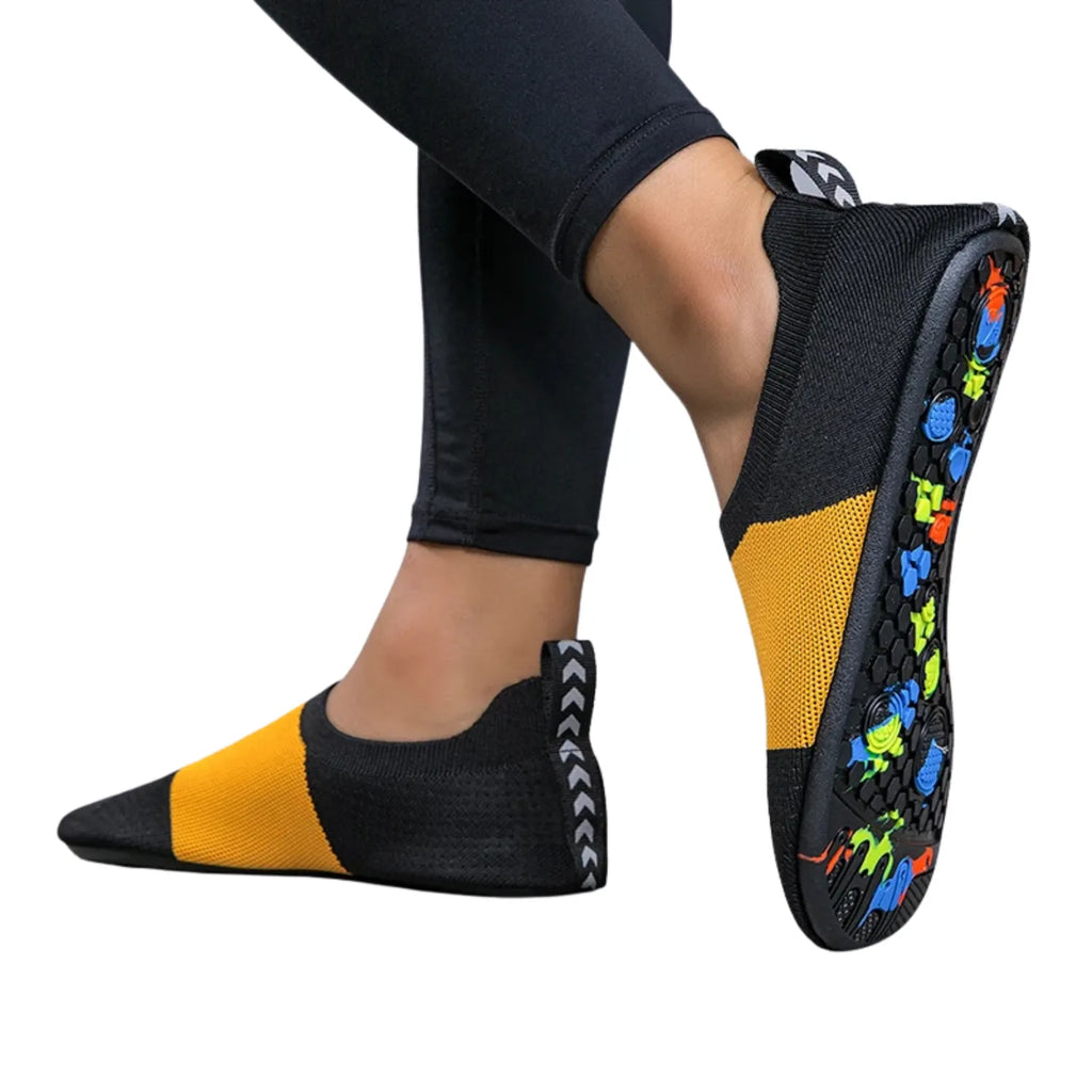 Pessoa usando um par de tênis de yoga. A sola do calçado tem uma textura antiderrapante e um padrão colorido vibrante.